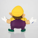 Action shot of the 6cm Wario figurine displayed on a gaming desk next to a Nintendo console setup.